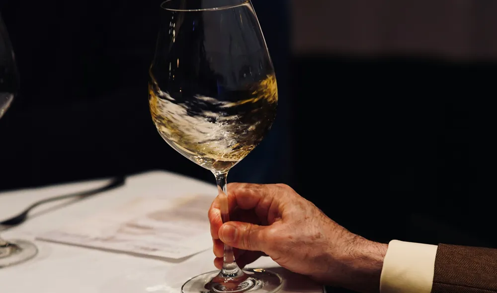 Un cliente di un locale tiene in mano un calice di vino bianco e lo fa girare prima di degustarlo